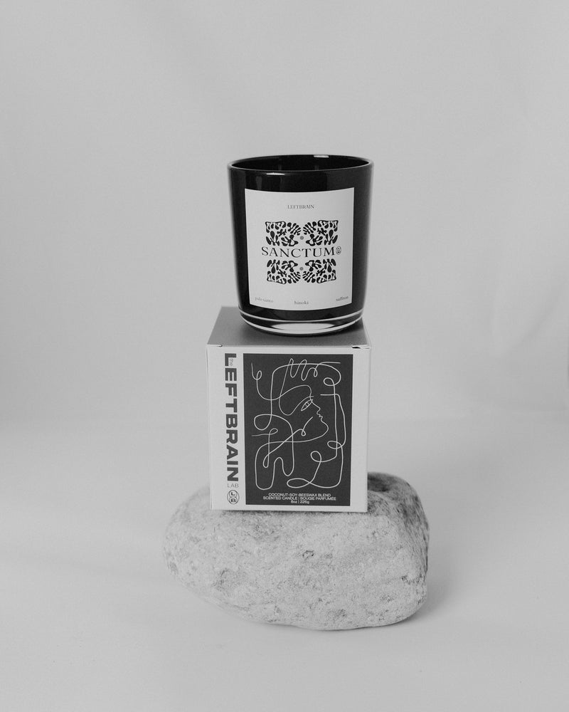 Hand-poured Sanctum Candle in black and white, posed on its designed box atop a rock, emphasizing its natural inspiration and calming home fragrance.