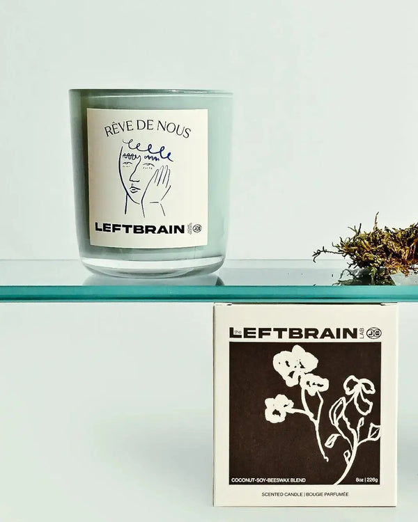 Hand-poured Rêve de Nous candle posed on its box on a shelf, showcasing its sea salt, pine, and cedar scent and subtle home fragrance.