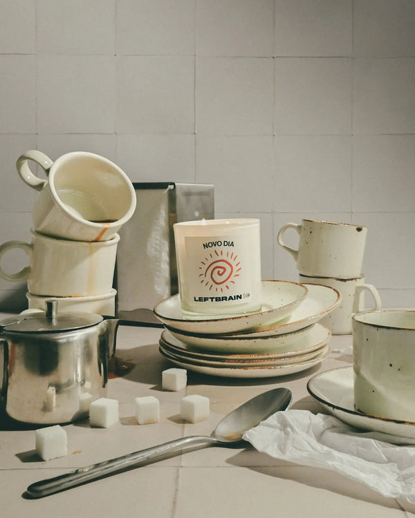 Hand-poured Novo Dia coffee-scented candle posed among coffee mugs in a casual diner-style setting, showcasing its cozy vibe and calming home fragrance.